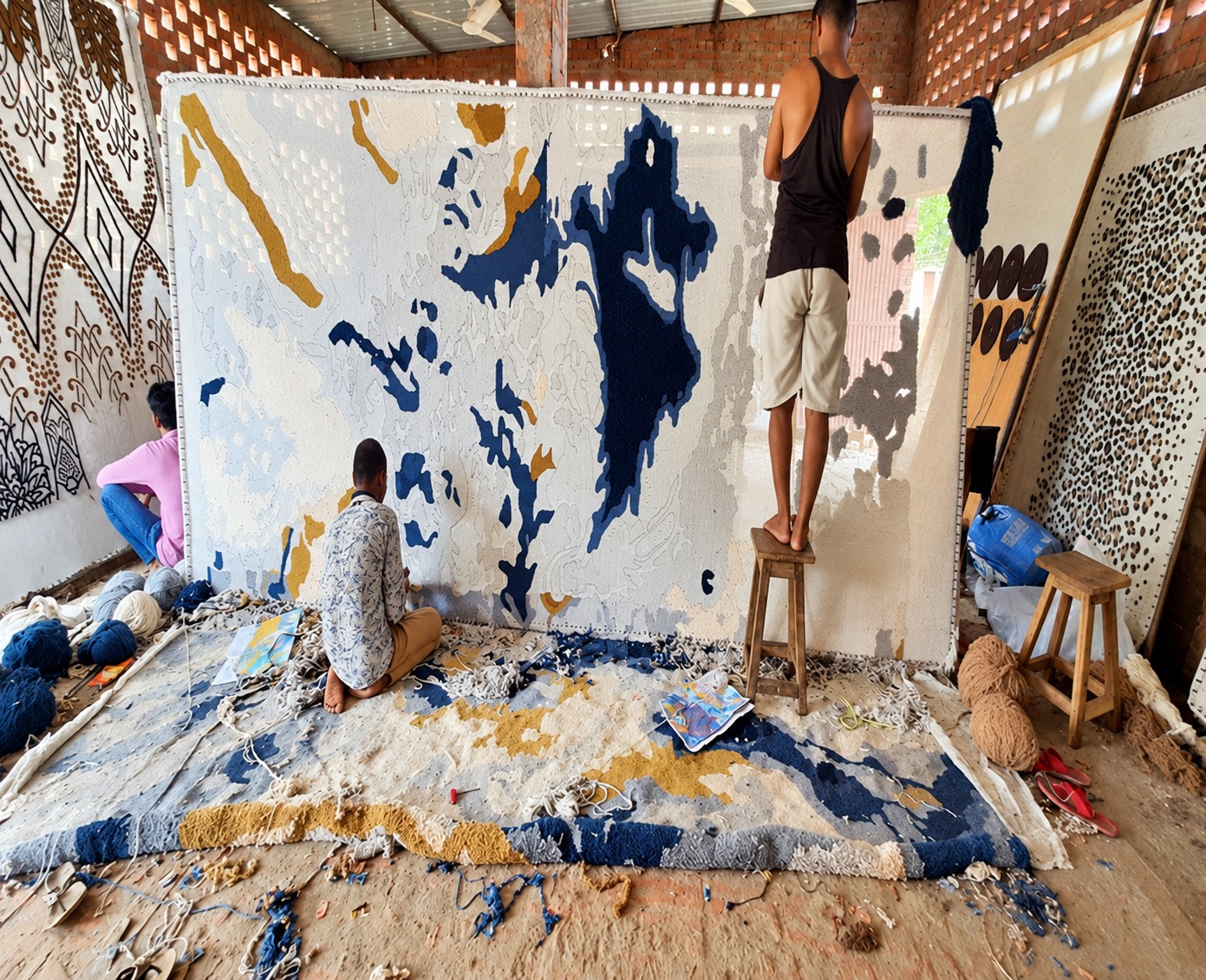 Artisans creating a large abstract rug on a tufting frame