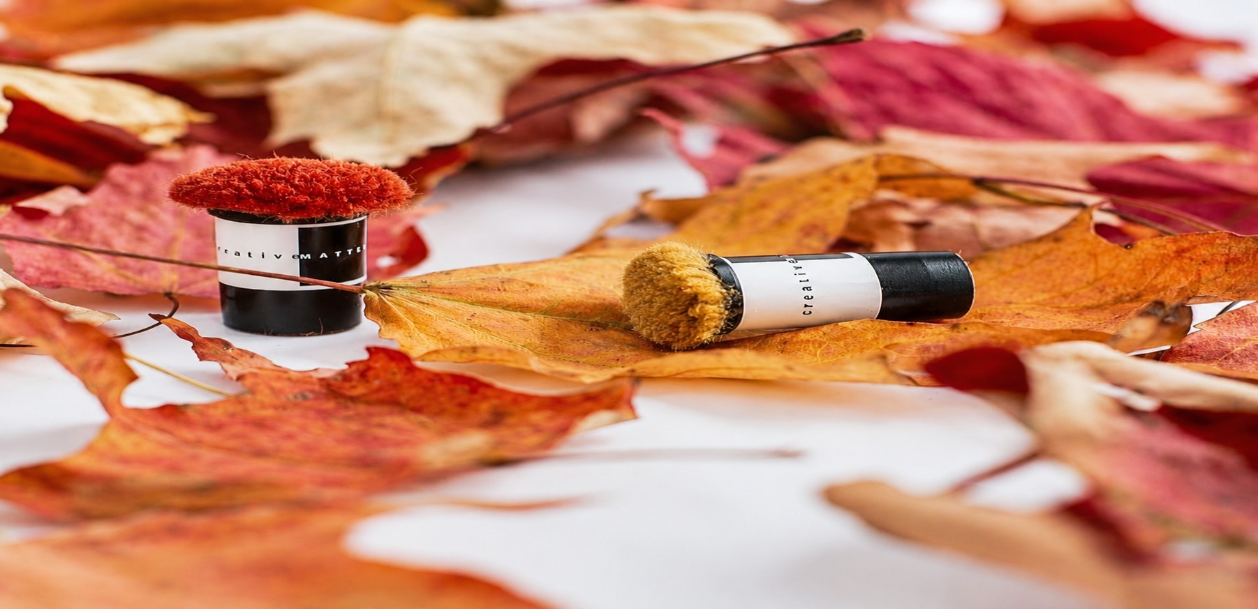 Red and mustard yarn colour samples beside autumn leaves